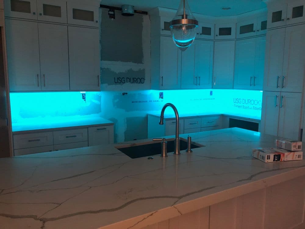 Modern kitchen with blue LED lighting, white cabinetry, and a marble countertop.