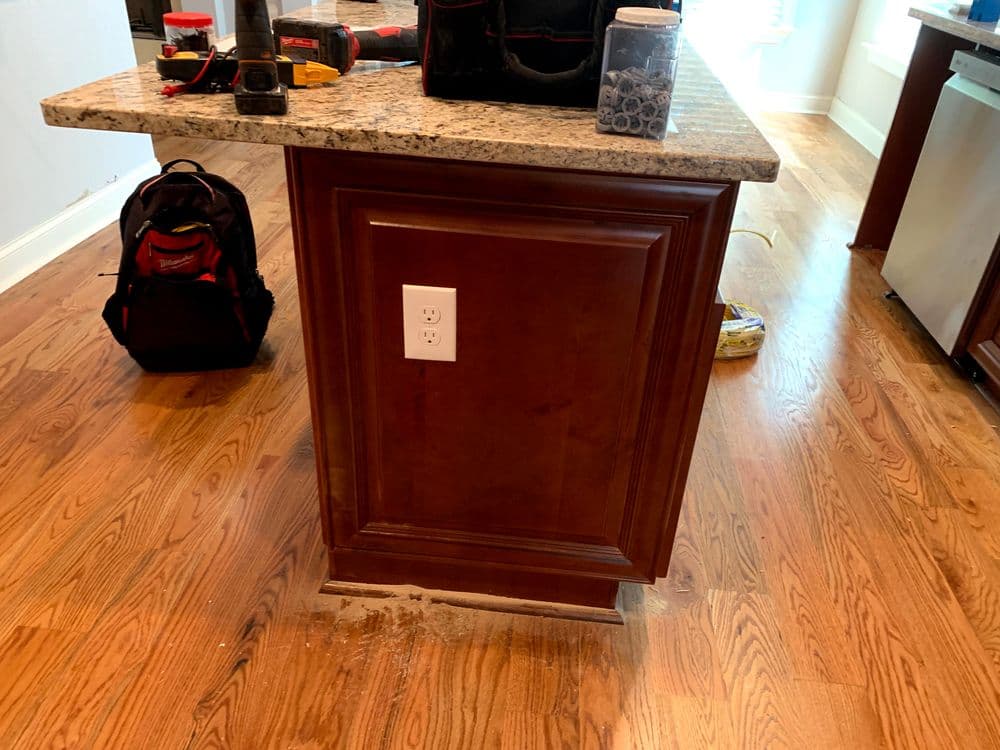 Kitchen island with granite countertop, electrical outlet, and construction tools nearby.